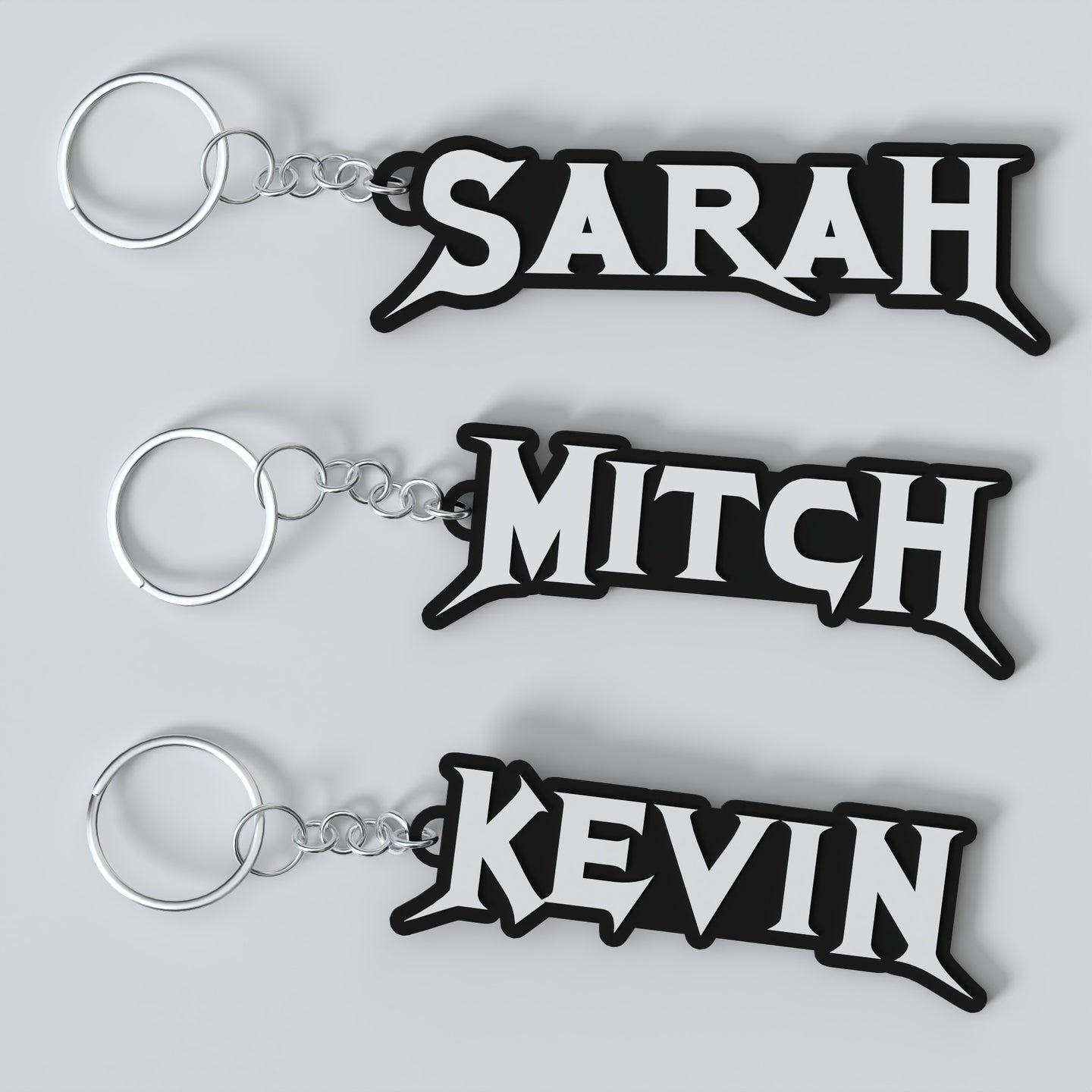 Three custom Megadeth keychains with the names 'Sarah', 'Mitch', and 'Kevin' printed on them, each keychain has a silver keyring and a chain link.