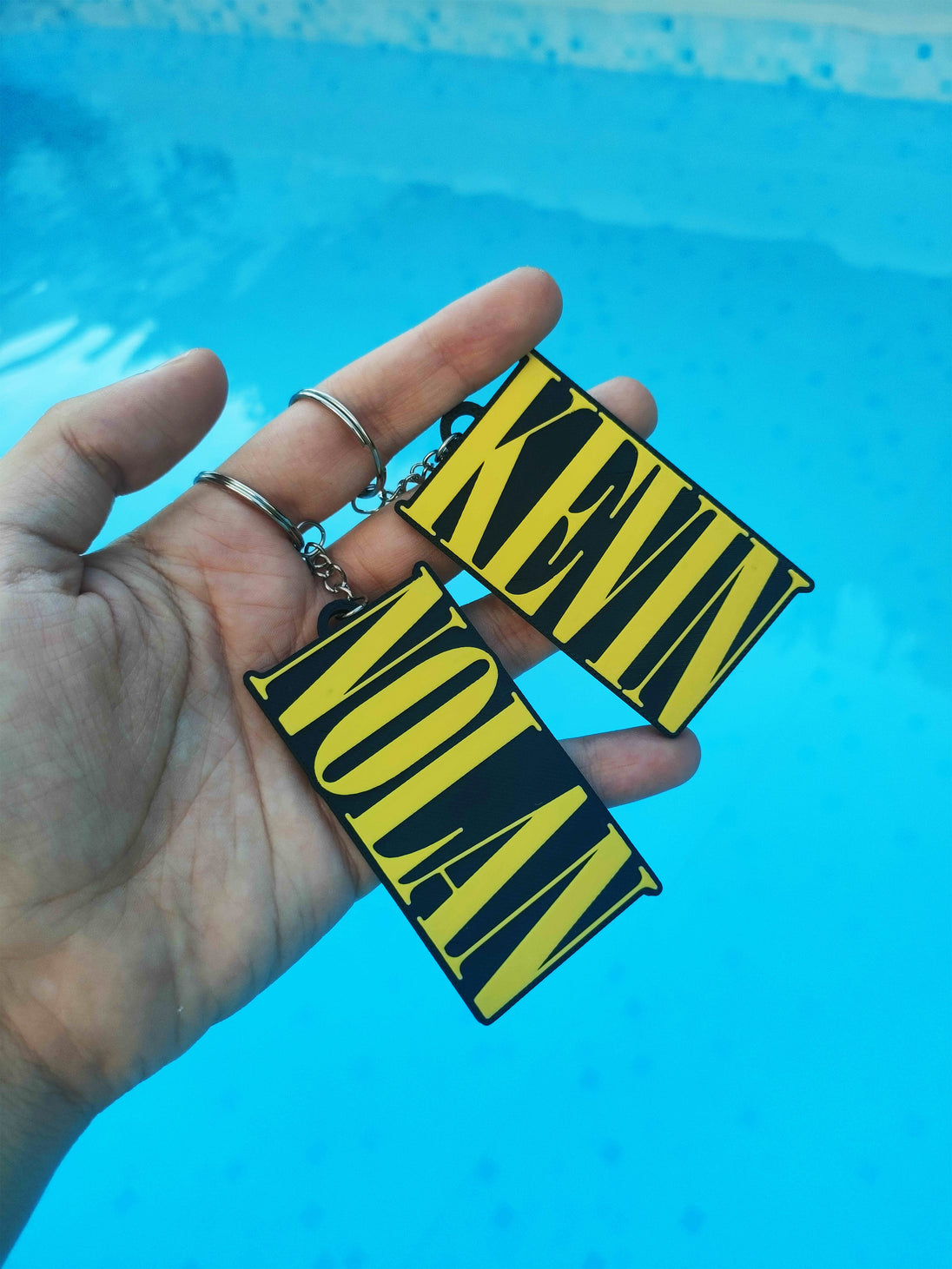 Custom Nirvana keychainS with the name "KEVIN" AND "NOLAN" in a man's hand, with a pool background.