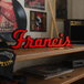 Wooden shelf with vinyl records, a guitar, and a 'Francis' Foo Fighters custom sign in a music-themed room.