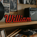 Wooden shelf with vinyl records, a guitar, and a 'William' Foo Fighters custom sign in a music-themed room.
