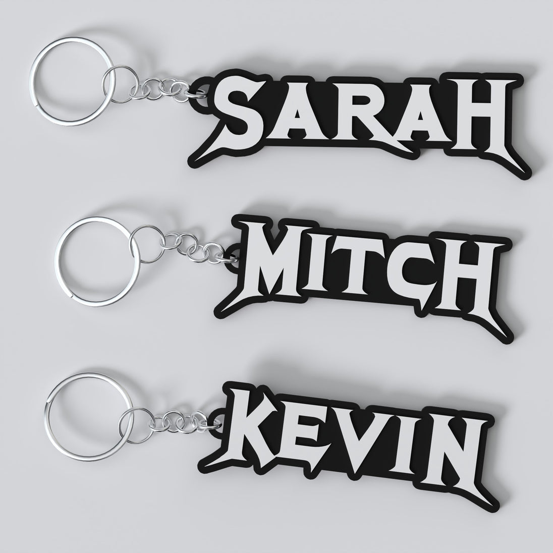 Three custom Megadeth keychains with the names 'Sarah', 'Mitch', and 'Kevin' printed on them, each keychain has a silver keyring and a chain link.