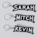 Three custom Megadeth keychains with the names 'Sarah', 'Mitch', and 'Kevin' printed on them, each keychain has a silver keyring and a chain link.
