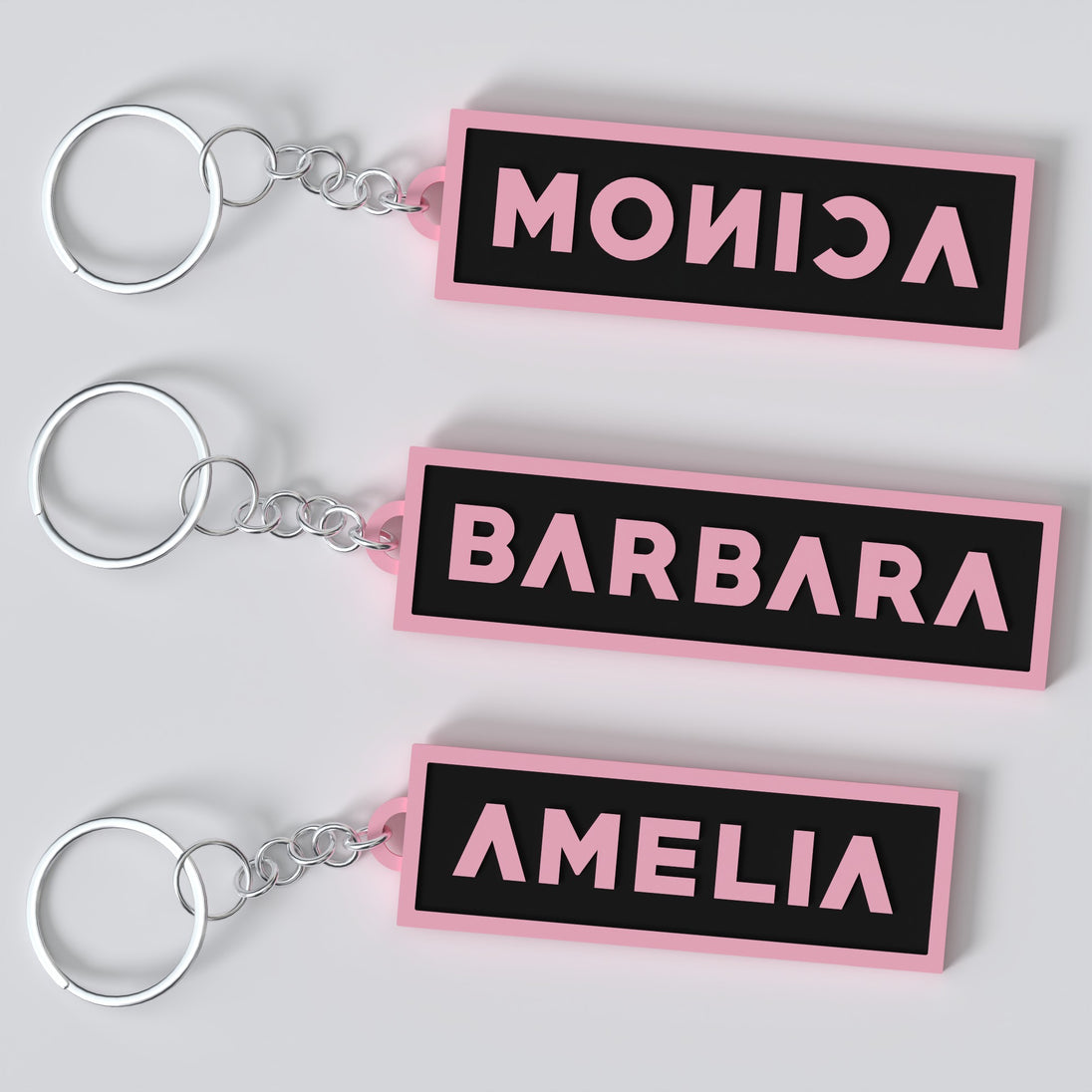 Black pink custom keychains with the names "MONICA", "BARBARA" AND "AMELIA".