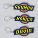 Custom anime-themed DIGIMON keychains with personalized engravings. One keychain reads 'AGUMON' with a blue and yellow font on a black background, and the other reads 'DAVID' with a similar color scheme.