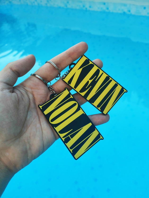 Custom Nirvana keychainS with the name "KEVIN" AND "NOLAN" in a man's hand, with a pool background.