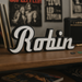 Wooden shelf with vinyl records, a guitar, and a 'Robin' Foo Fighters custom sign in a music-themed room.